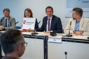 Ministerpräsident Olaf Lies, Vize-Ministerpräsident Julia Hamburg und der lachende Finanzminister Gerald Heere zeigen während der Landespressekonferenz ein Plakat hoch mit der Aufschrift: "Niedersachen kann Zukunft"