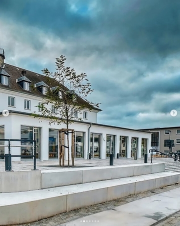 das Gebäude aus einer anderen Sicht schräg nach rechts mit Treppe, Baum und großen Fenstern