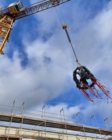 der Richtkranz hängt am Kran. Er schwankt über dem Rohbau mit Gerüst.