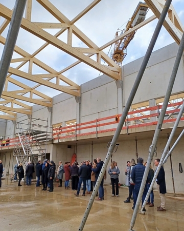 eine große Gruppe Menschen ist im Rohbau zu sehen. Man sieht teile vom Gerüst und ein Kran, der über dem Dach zu schweben scheint