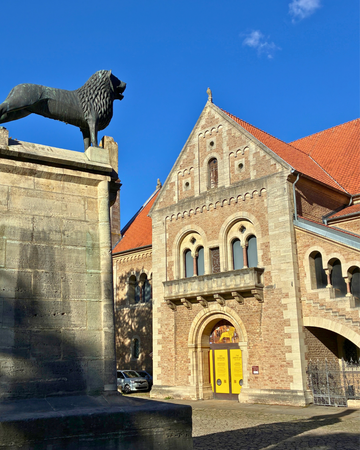 Das Bild zeigt die Burg mit Eingang. Im Vordergrund ist der Löwe von Braunschweig zu sehen, der gegenüber vom Eingang der Burg steht. Die sonne scheint auf das helle Mauerwerk