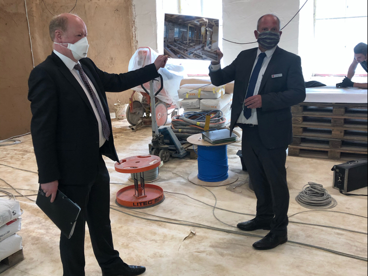 Minister Hilbers und der Leiter des Staatlichen Baumanagements Südniedersachsen Marcus Rogge zeigen auf der Baustelle ein Bild des ursprünglichen Zustands des Raumes