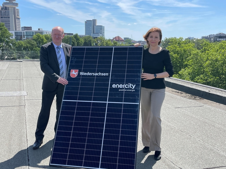 Minister Reinhold Hilbers und Dr. Susanna Zapreva mit einer Photovoltaikplatte auf einem Dach