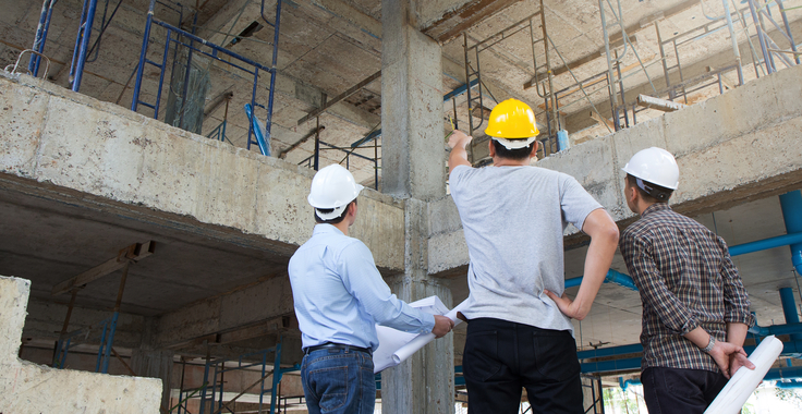 3 Architekten oder Bauingenieure stehen mit Bauzeichnungen in einem Rohbau