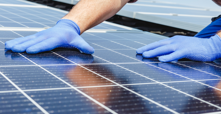 Hände mit Schutzhandschuhen in Nahaufnahme, die ein PV-Modul platzieren