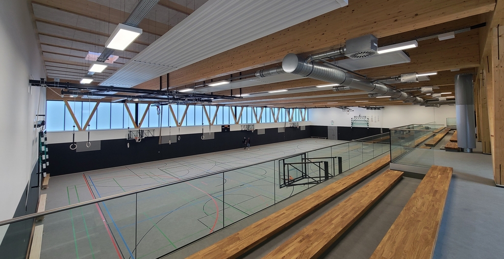 Blick von der Zuschauertribüne in eine großzügige Sporthalle mit vielen Holzelementen