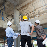 3 Architekten oder Bauingenieure stehen mit Bauzeichnungen in einem Rohbau